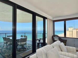 Un balcon avec vue sur l’océan et les bâtiments, aménagé avec un canapé et des fauteuils.