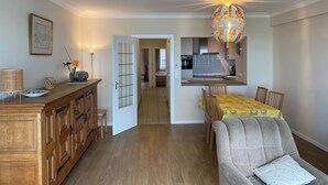 A modern living room with a dining area, wooden furniture, and a kitchen in the background. - Apartment in Nieuwpoort by the Beach (Nieuwpoort)