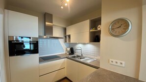 A modern kitchen with white cabinets, a built-in oven, a sink, and a clock on the wall. - Apartment in Nieuwpoort by the Beach (Nieuwpoort)