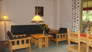 A cozy room with a wooden sofa, two wooden chairs, a small table, and a lamp. - Mrs. Monika Rasehorn (Altenberg)