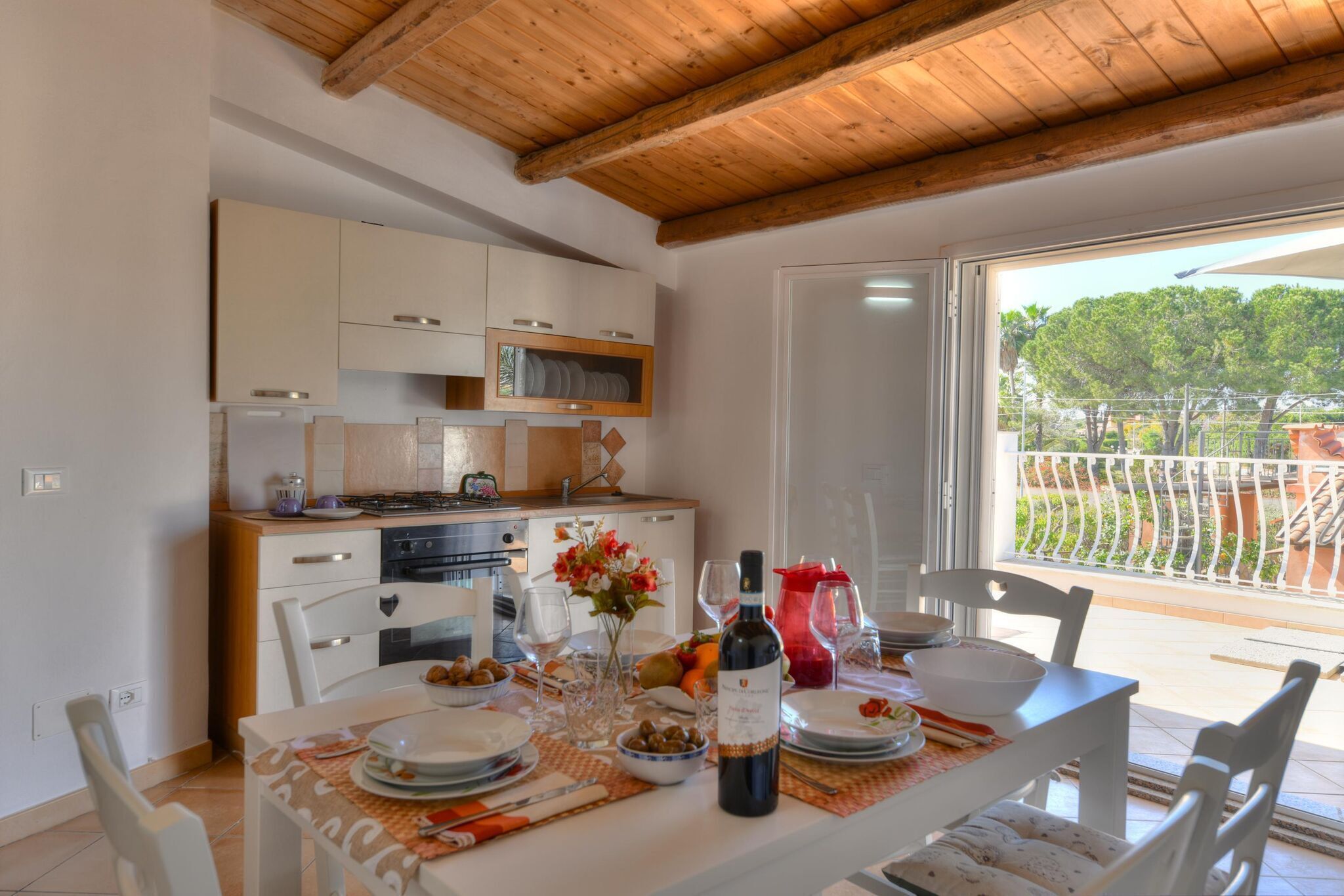 Un coin repas avec une table mise pour le dîner, une cuisine en arrière-plan et une vue sur un balcon doté d’une balustrade.