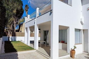 A modern white house with a covered patio, a small lawn, and a potted plant. - Nice Apartment with Pool (Siracusa)