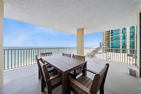 Un balcon doté d’une table et de chaises en bois, offrant une vue sur une plage et un immeuble avec des balcons.