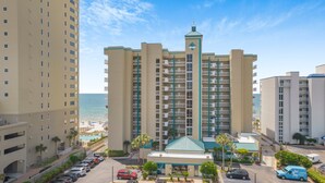 A multi-story hotel with a central tower, a pool area, and a parking lot. - 🌊 Romar Place 1106 | Top Floor Gulf Front | Corner Balcony + Resort Amenities (Orange Beach)