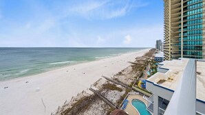 A beach view from a hotel with a pool and a high-rise building in the background. - 🌊 Romar Place 1106 | Top Floor Gulf Front | Corner Balcony + Resort Amenities (Orange Beach)