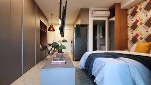 A modern hotel room with a bed, bedside table, and a small seating area. There is a wardrobe, a desk, and a potted plant. - Vossa Bossa Setin República (São Paulo)
