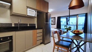 A modern kitchen with a built-in oven, microwave, and refrigerator. There is a dining area with a table and chairs, and a view of the city through large windows. - Vossa Bossa Setin República (São Paulo)