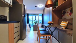 A modern kitchen with a refrigerator, dining table, and chairs. There is a window with a view of buildings outside. - Vossa Bossa Setin República (São Paulo)