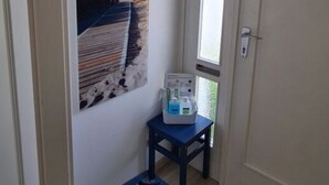 Un pasillo con un cuadro de una escena de playa, una mesita con una computadora portátil y una puerta con ventanal.