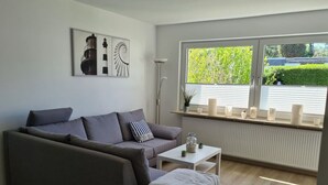 Una sala de estar moderna con un sofá gris, una mesita blanca y una ventana con persianas.