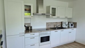 Una cocina moderna con gabinetes blancos, horno empotrado, campana extractora de acero inoxidable, pileta y cafetera.
