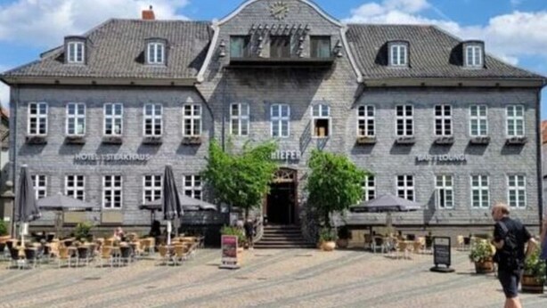 Un edificio histórico con entrada central, múltiples ventanas y zonas de estar al aire libre.