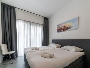 A modern hotel room with two beds, a chair, and a painting of a cityscape.