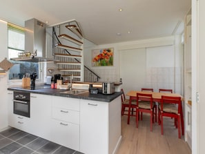 A modern kitchen with a central island, a dining area with red chairs, and a staircase leading to an upper level. - Holiday Home in Koudekerke With Hot Tub (Koudekerke)