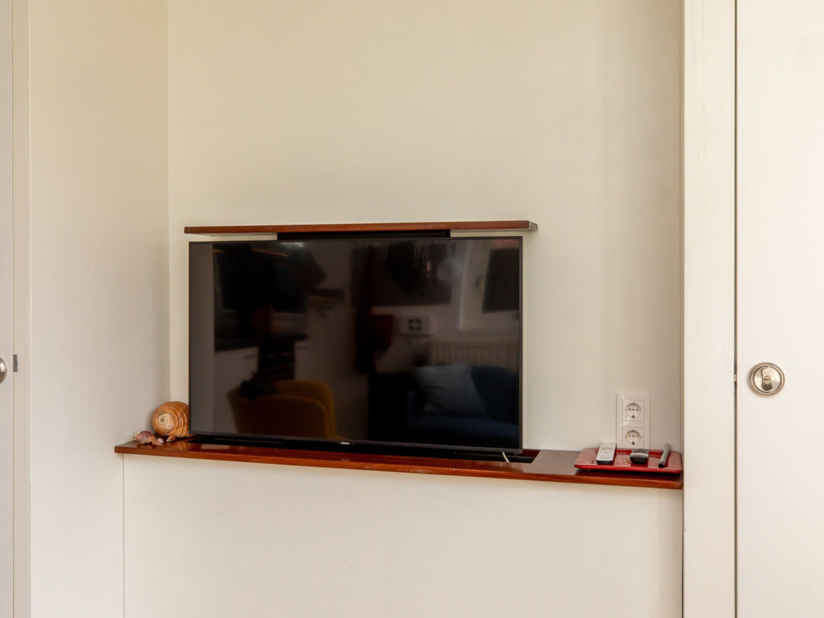 A television mounted on a wall with a wooden shelf below.