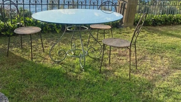 A round glass table with metal chairs and a statue, set against a coastal backdrop. - 3 Bedroom Apartment in Massa Lubrense (Massa Lubrense)