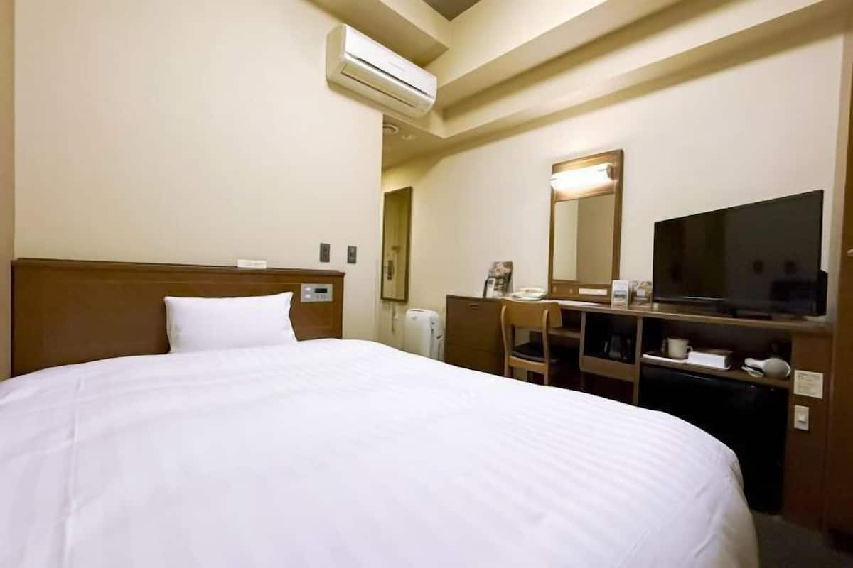 Ein Hotelzimmer mit einem großen Bett, einem Schreibtisch mit Stuhl, einem Fernseher und einer Klimaanlage.