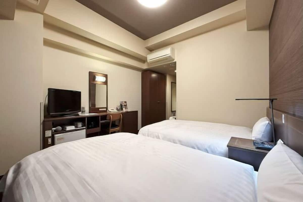 Ein Hotelzimmer mit zwei Betten, einem Schreibtisch mit Fernseher, einem Spiegel und einem Kleiderschrank.
