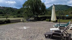 A patio with stone flooring, a large tree, and a mountain in the background.