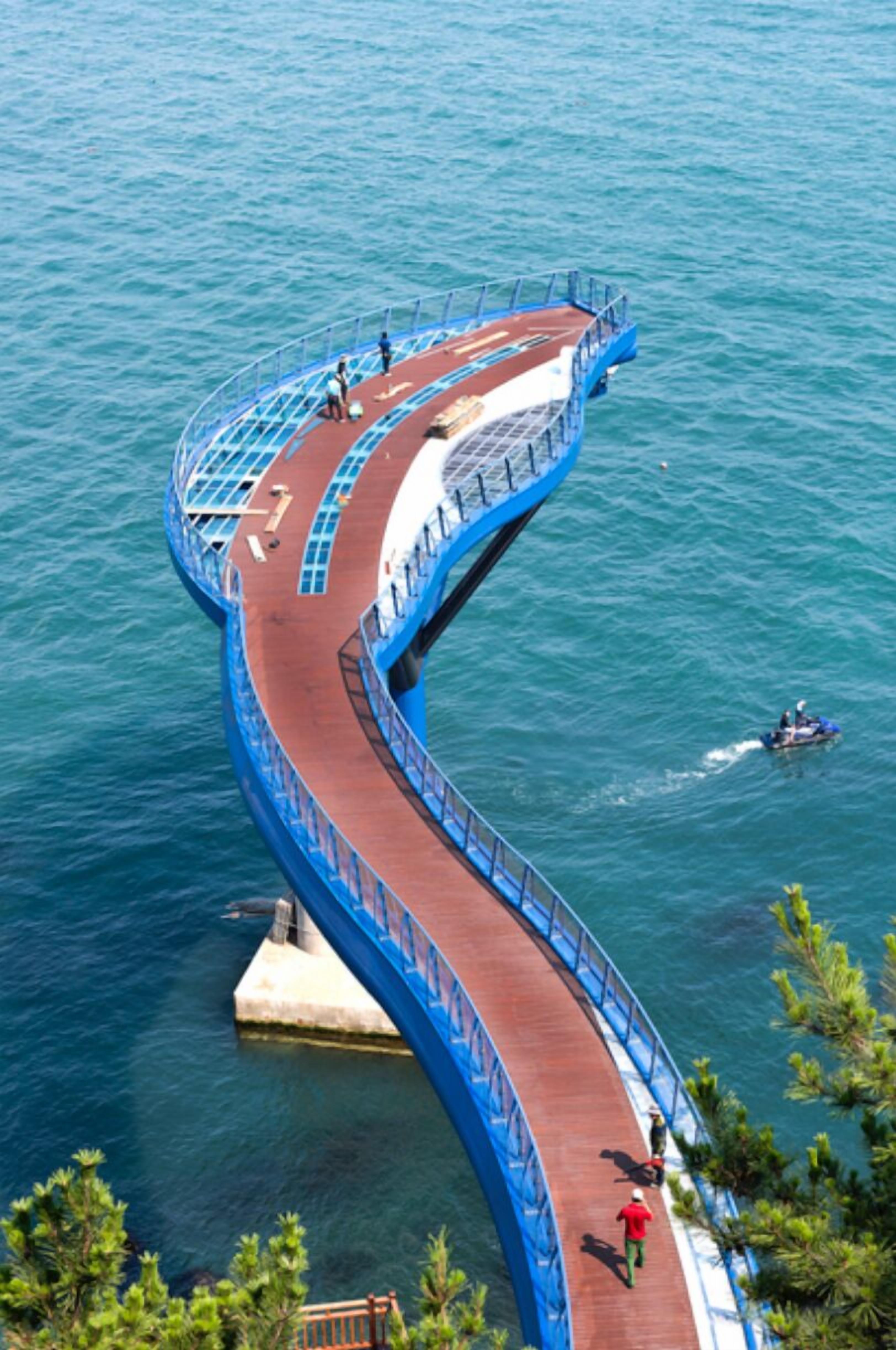 Un puente peatonal curvo sobre el agua, con gente caminando y una embarcación cerca.