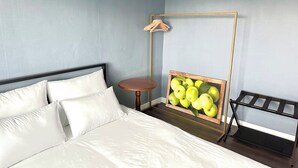 Un lit bien fait, avec du linge de lit blanc, une table ronde en bois et un porte-manteau en bois fixé au mur.