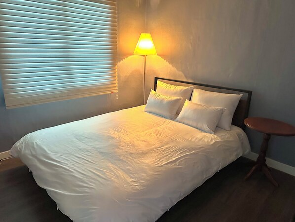 A neatly made bed with white linens, a bedside lamp, and a small round table beside it. - blackkoi stay (Busan)