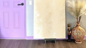 Une pièce avec une porte violette, une grande œuvre d’art encadrée au mur, un vase décoratif et une petite figurine.