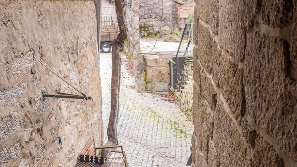A narrow cobblestone alley with stone walls, a metal bench, a small table, and a potted plant. - GerêsTER  (Terras de Bouro)