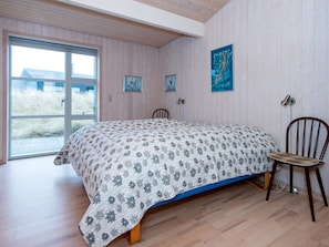 A bedroom with a bed, a chair, wooden flooring, a window, and wall-mounted artwork. - 5 Star Holiday Home in Henne (Henne)