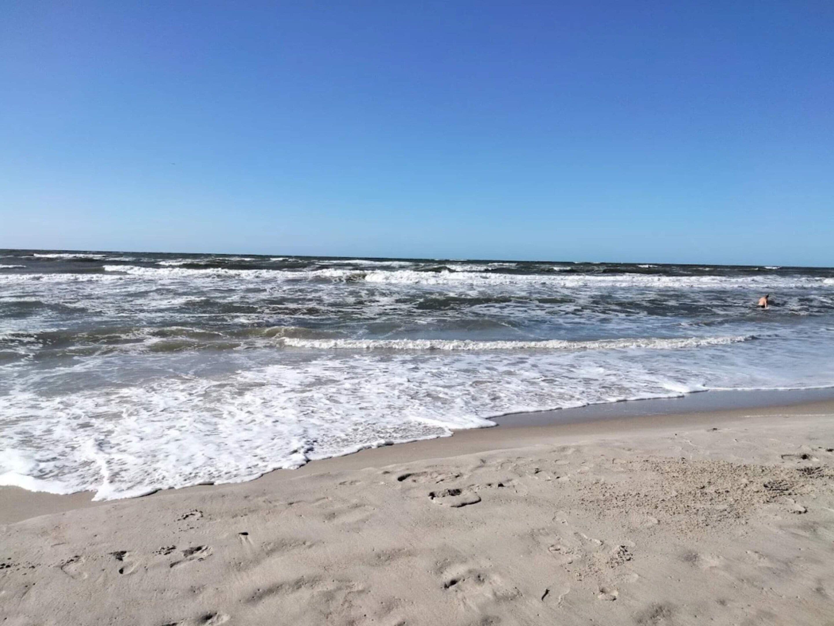 A beach with waves, a clear sky, and footprints in the sand.