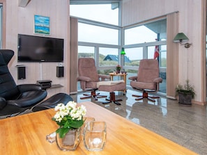 A modern room with a large TV, two leather chairs, a wooden table, and a view of the outdoors. - 5 Star Holiday Home in Henne (Henne)