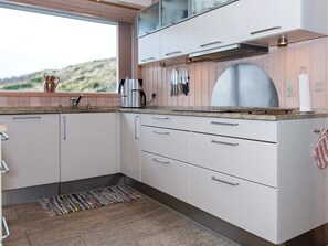 A modern kitchen with white cabinets, stainless steel appliances, and a large window overlooking a grassy hill.