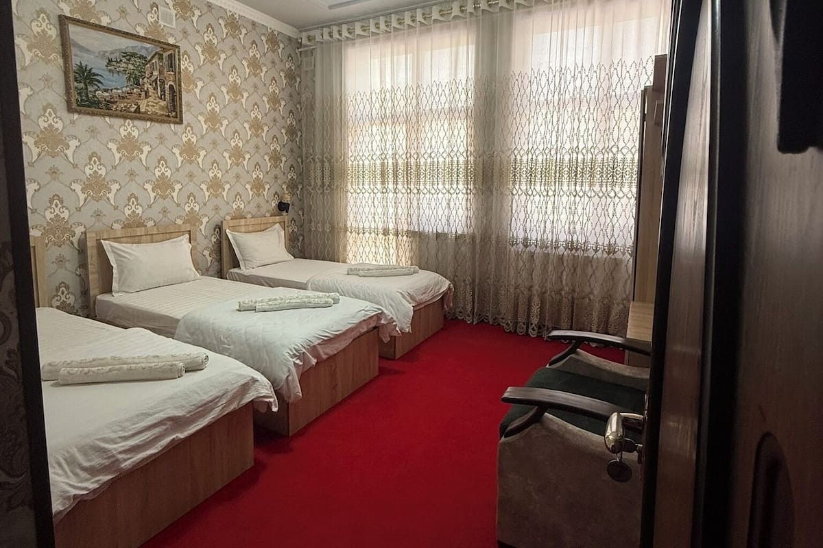 A hotel room with three beds, a red carpet, a ceiling light fixture, and a painting on the wall.