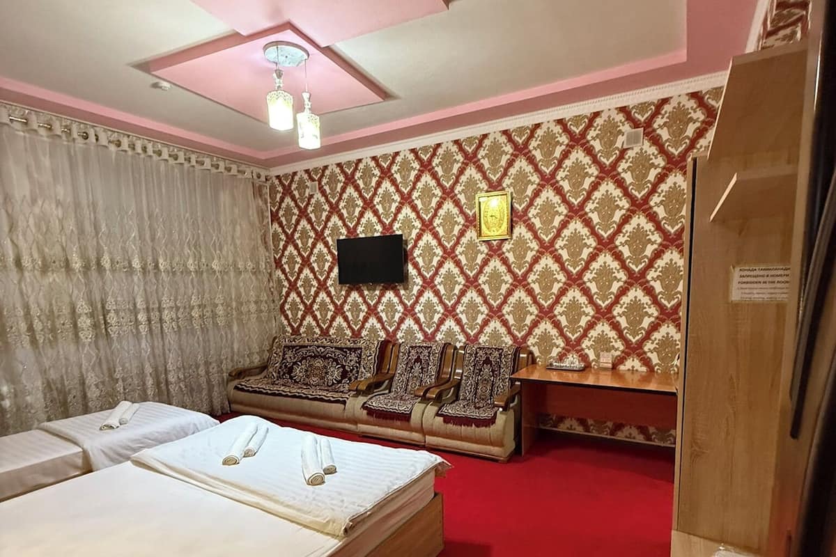 A bedroom with a large bed, a sofa, a TV, and patterned wallpaper.