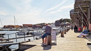 A wooden pier with boats docked, a signboard, and buildings in the background. - 6 Person Holiday Home in Skjaerhalden (Hvaler)