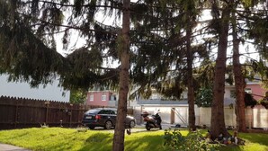 Zona residencial con camino pavimentado, un auto estacionado, una motocicleta y un árbol pequeño.