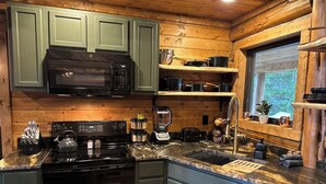Une cuisine équipée d’une cuisinière, d’un four à micro-ondes et de divers appareils électroménagers. On y trouve des placards en bois et une fenêtre donnant sur un paysage verdoyant.