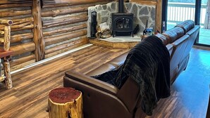 L’intérieur d’une cabane en rondins, avec une cheminée en pierre, un téléviseur fixé au mur et un canapé en cuir.
