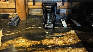 Une cuisine rustique aux murs en bois, avec une machine à café et des ustensiles de cuisine noirs rangés sur des étagères.