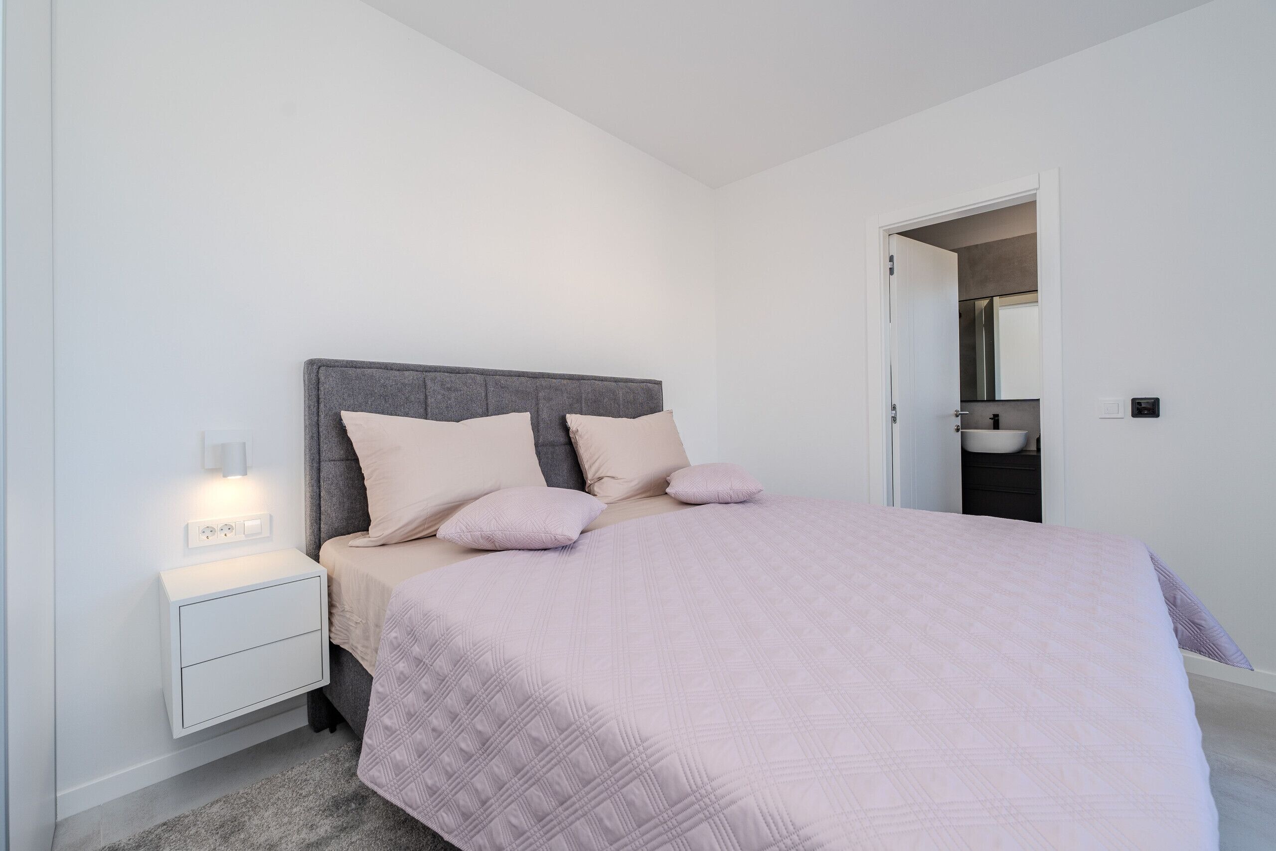 Un dormitorio con cama, mesita de noche y baño visible a través de una puerta abierta.
