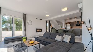 Una sala de estar moderna con un sofá seccional, una mesa de centro con fruta, y vistas a la cocina y la escalera.