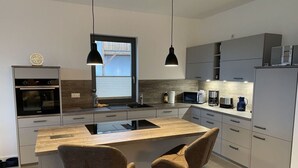 A modern kitchen with a central island, two bar stools, a built-in oven, a microwave, and a refrigerator. - Uitzicht op de Kraanvogel (Dreschvitz)