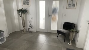 A spacious room with a grey tiled floor, a dark grey armchair, a tall vase with plants, and a door with frosted glass panels. - Uitzicht op de Kraanvogel (Dreschvitz)