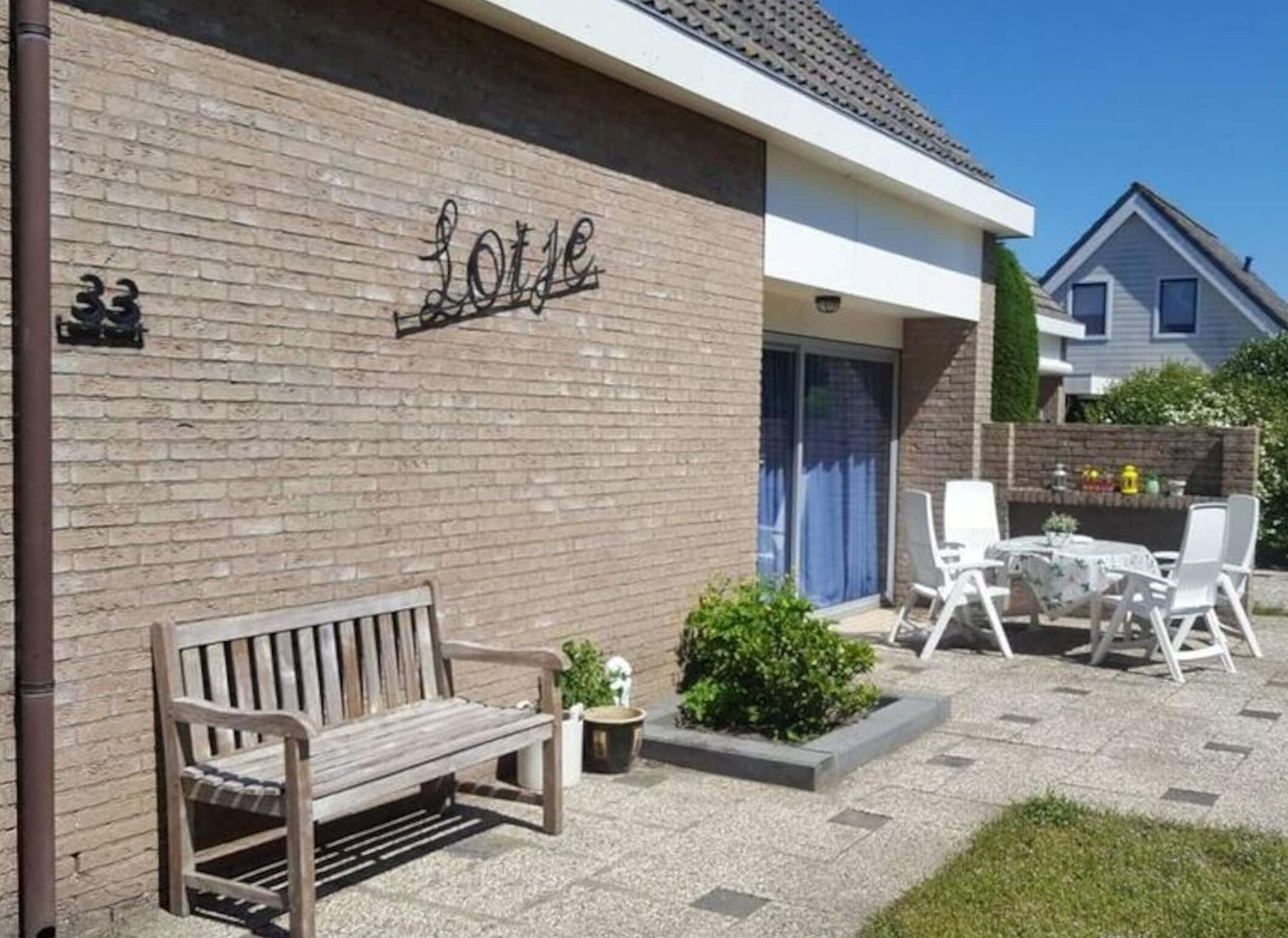 A building with a brick facade and the word "Lotte" on the wall. There is a wooden bench and outdoor seating with white chairs and a table.