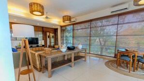 Una sala de estar moderna con una mesa de comedor de madera, un televisor y un ventanal con persianas.