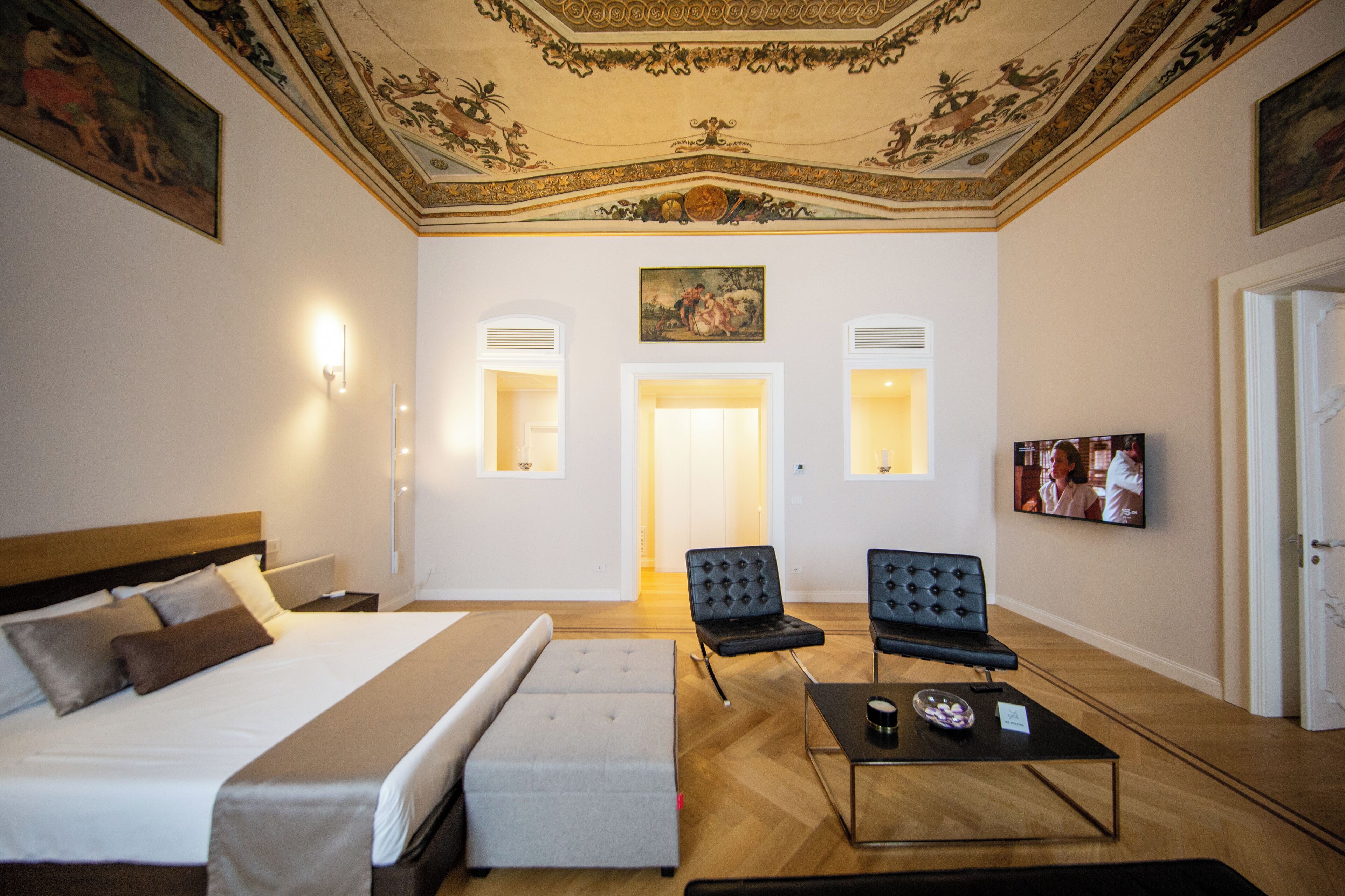 A hotel room with a large bed, two armchairs, a coffee table, and a television.