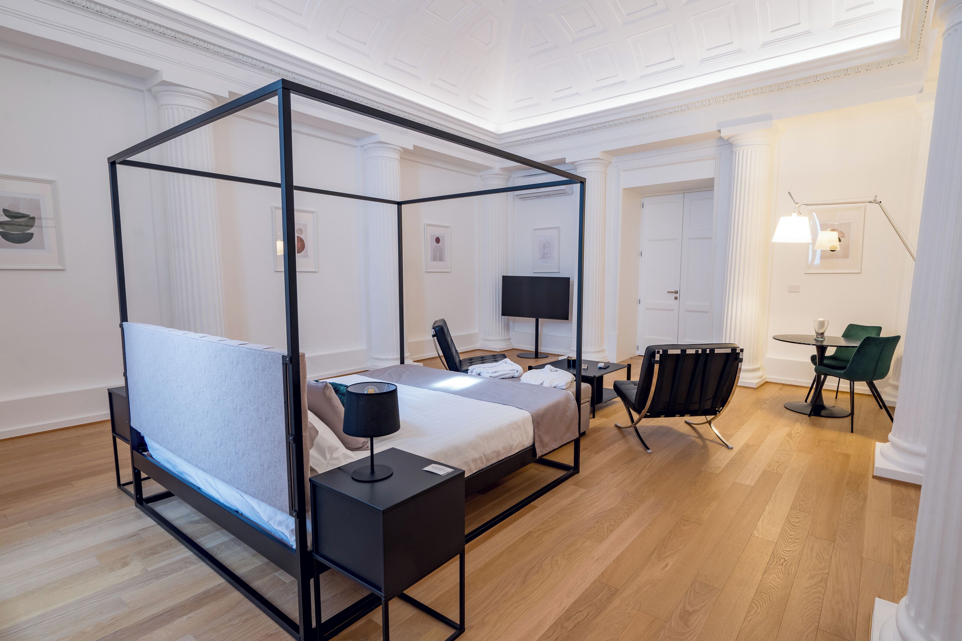 Une chambre d’hôtel moderne dotée d’un lit à baldaquin, d’un bureau avec une chaise, d’une télévision à écran plat et d’un coin repas avec une table et des chaises.