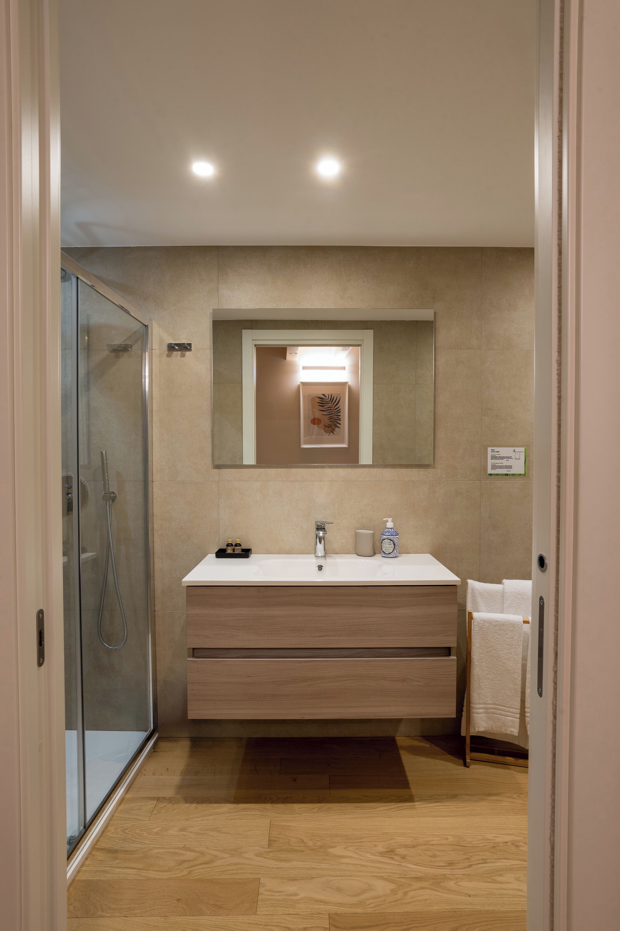 Un baño moderno con cabina de ducha de vidrio, tocador de madera con espejo y lavabo blanco.