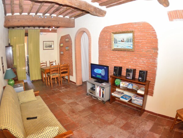 A living room with a television, speakers, and a bookshelf. There is a dining area with chairs and a table.