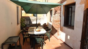 Een klein terras met een tafel en stoelen onder een groene parasol, omringd door gebouwen.